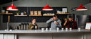 Three people sitting at a counter with coffee cups in a modern kitchen setting.